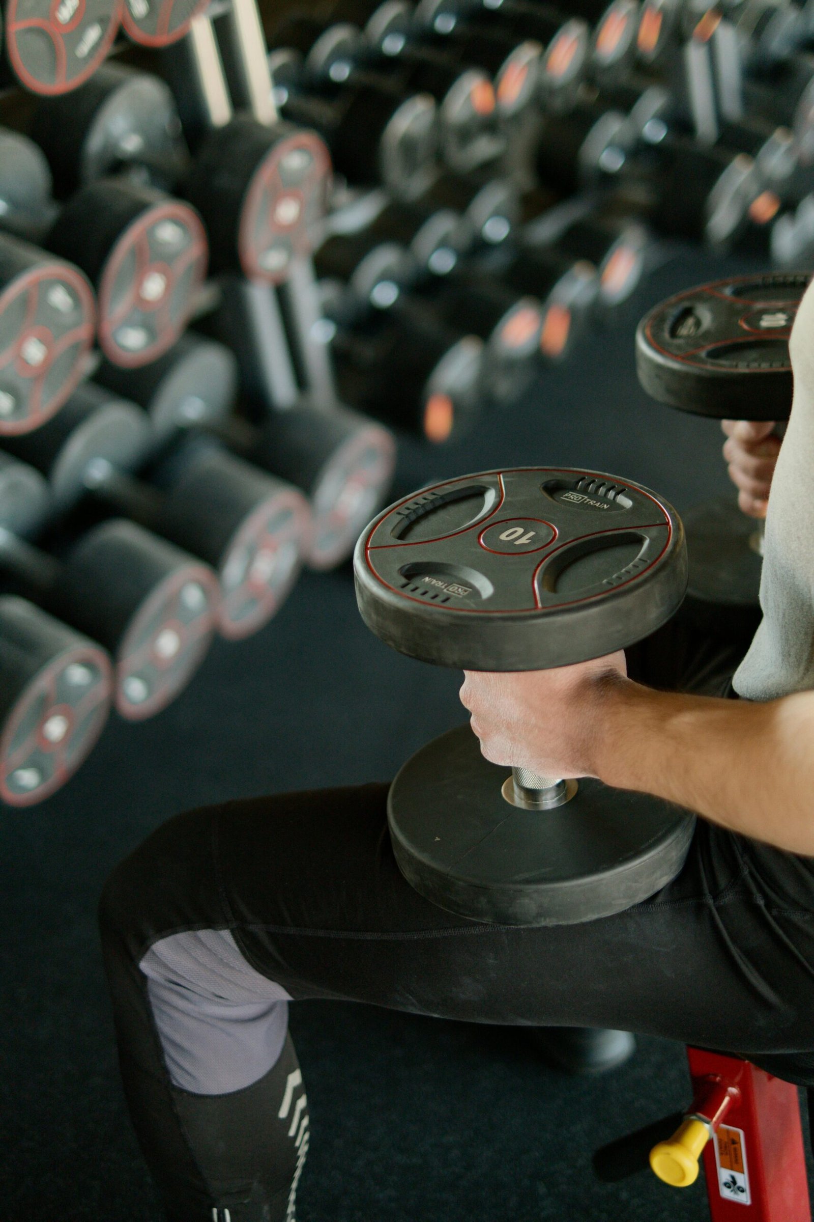 A guy sitting in a gym holding dumbbells on his lap