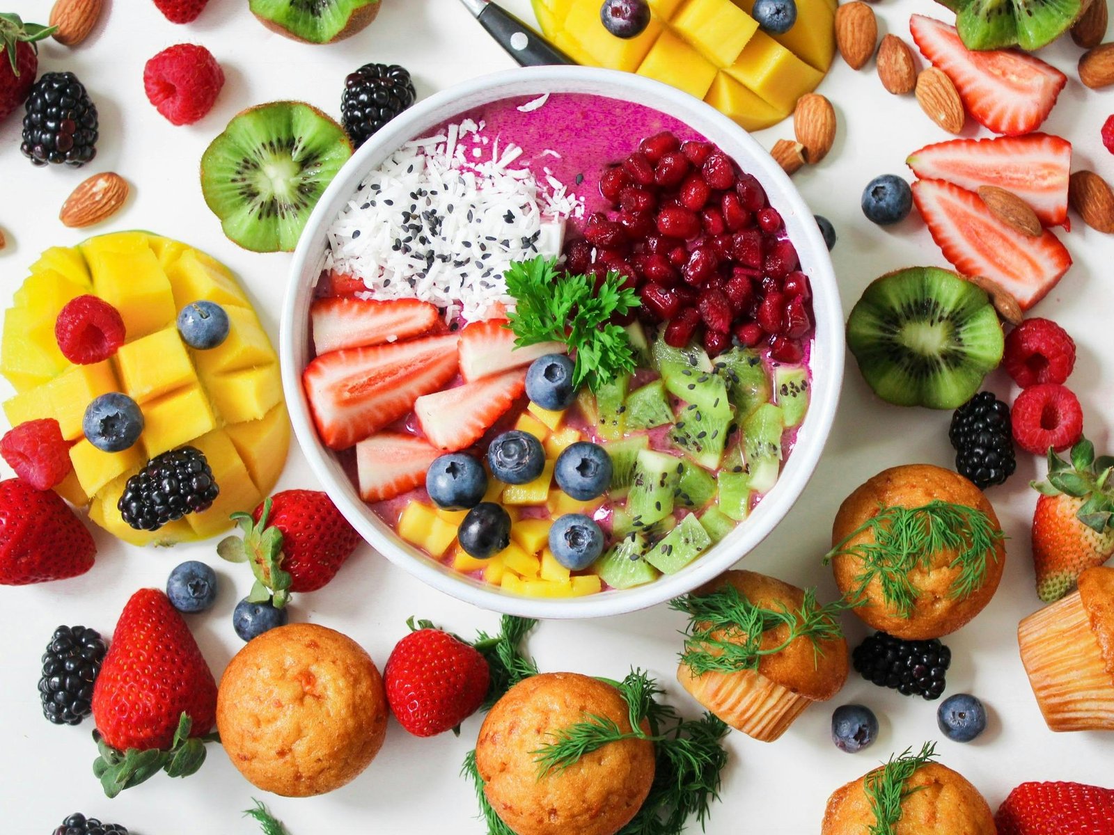 A bowl of healthy fruits & fruit all over a white table